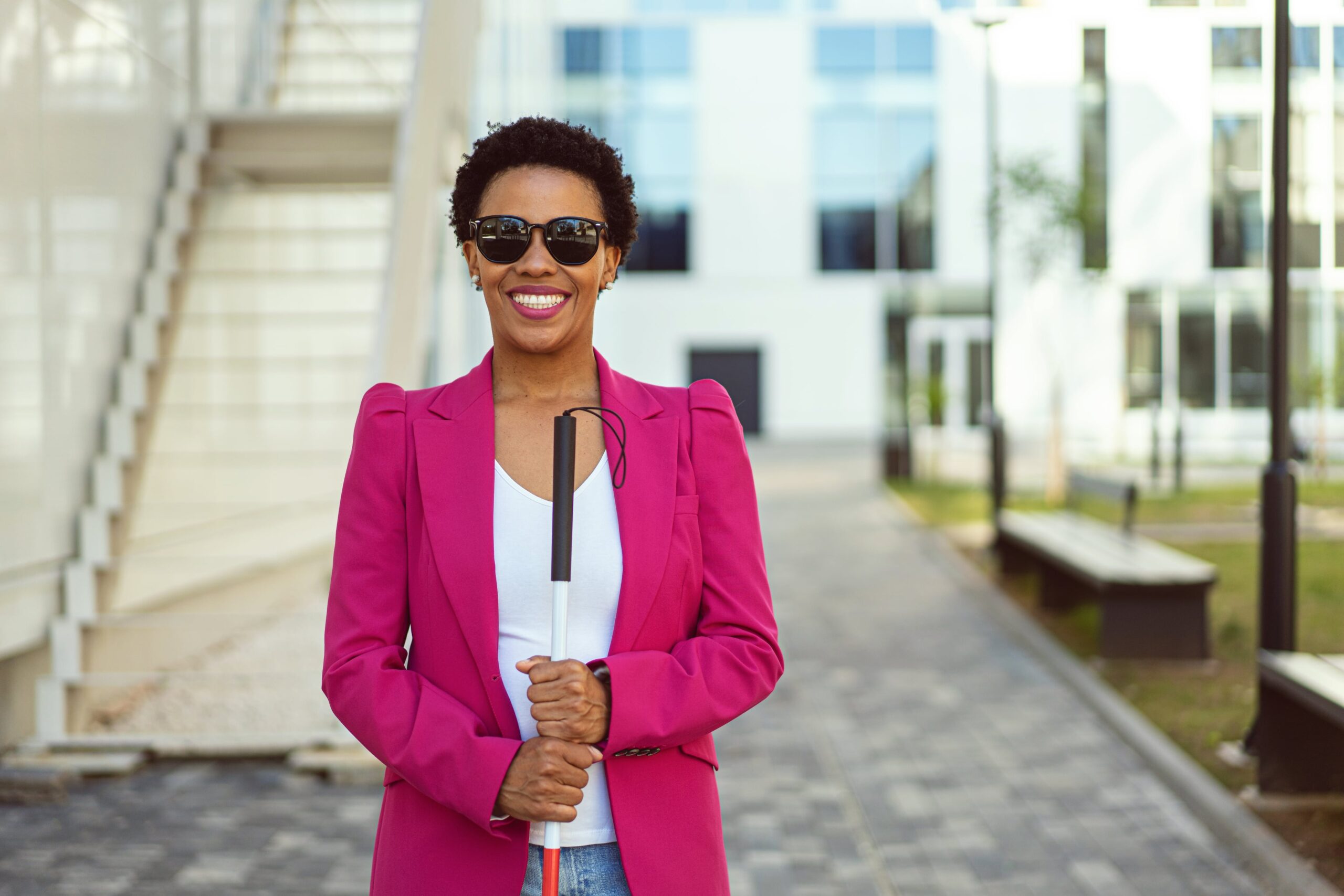 A woman wearing sunglasses, smiling, holding a white cane